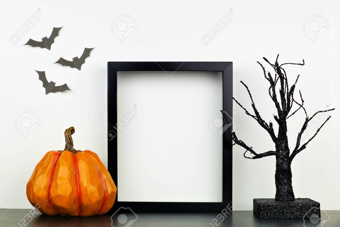 Mock up black frame with Halloween pumpkin and spooky tree decor on a shelf against a white wall - 130017182 Mock up black frame with Halloween pumpkin and spooky tree decor on a shelf against a white wall - 130017182