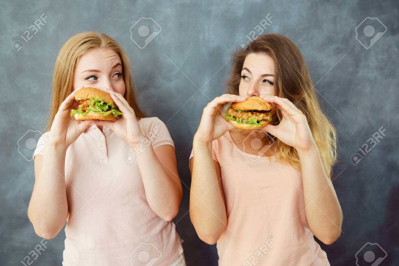 Two Women Eating Burgers And Look At Each Other Stock Photo, Picture and  Royalty Free Image. Image 106159724.