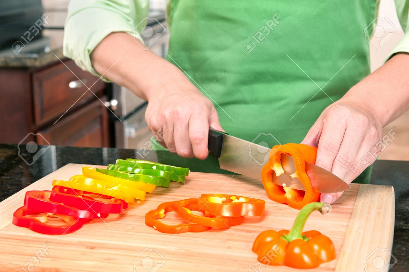 a woman slicing bell peppers prepares the vegetables as meal stock