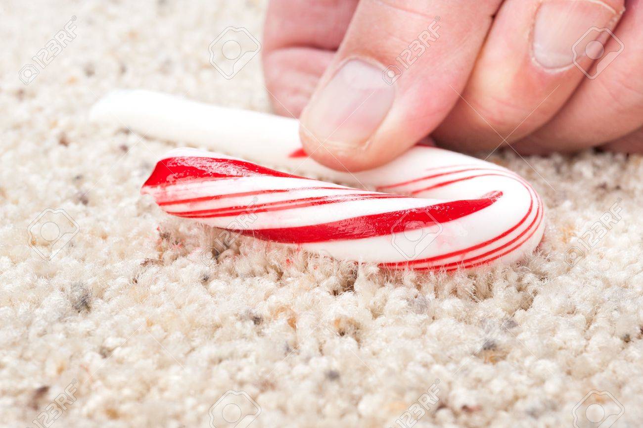 A man picks up a dropped candy cane that is stick to carpet fibers. - 11199719 A man picks up a dropped candy cane that is stick to carpet fibers. - 11199719
