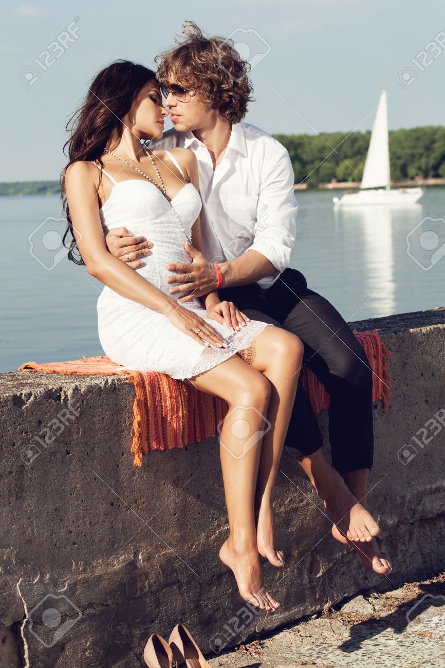 セクシーな素敵なカップル夏の桟橋に暑い太陽の下でキスします 若い男と古典的なドレスで官能的なブルネット屋外のポートレートの海の近くです アウトドア ライフ スタイル の写真素材 画像素材 Image