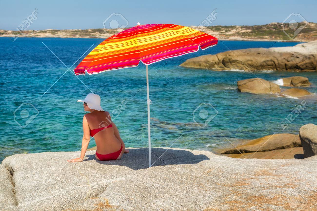 mujer en bikini rojo y sombrero grande disquete blanco sentado bajo una sombrilla de rayas - Sombrillas De Playa Grandes mujer en bikini rojo y sombrero grande disquete blanco sentado bajo una sombrilla de rayas - Sombrillas De Playa Grandes