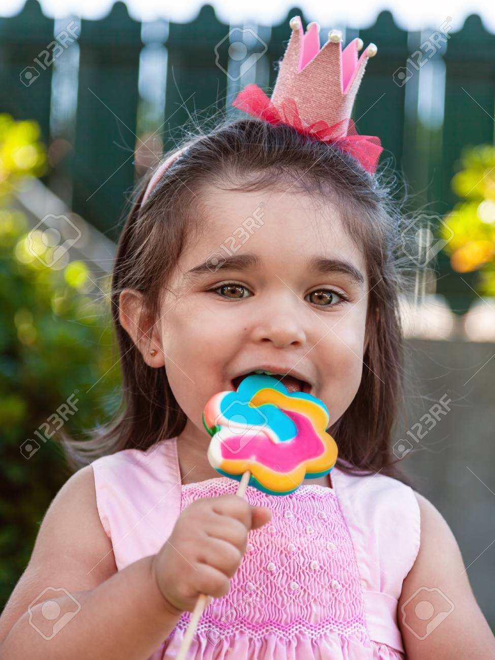 Happy Baby Toddler Girl Eating And Biting A Large Colorful Lollipop