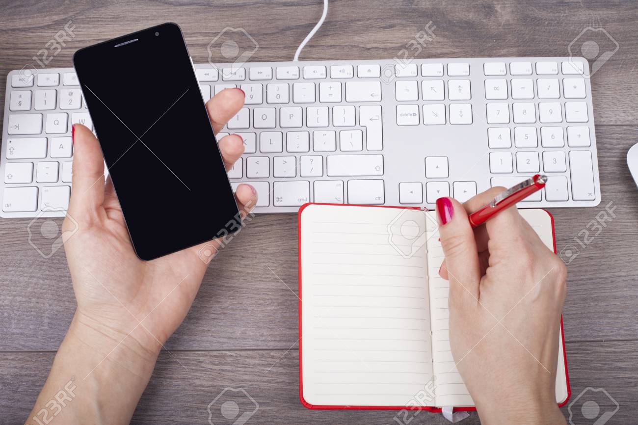 Closeup Da Mao Feminina Escrevendo Em Um Caderno E Usar Um Telefone Celular Na Mesa Com Um Teclado Fotos Retratos Imagenes Y Fotografia De Archivo Libres De Derecho Image 72555659