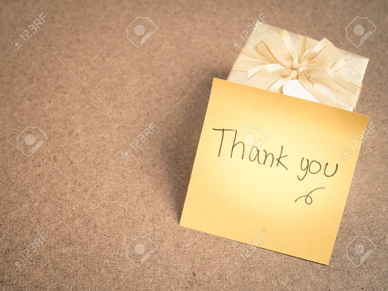 hand writing thank you words on yellow sticky note with gold