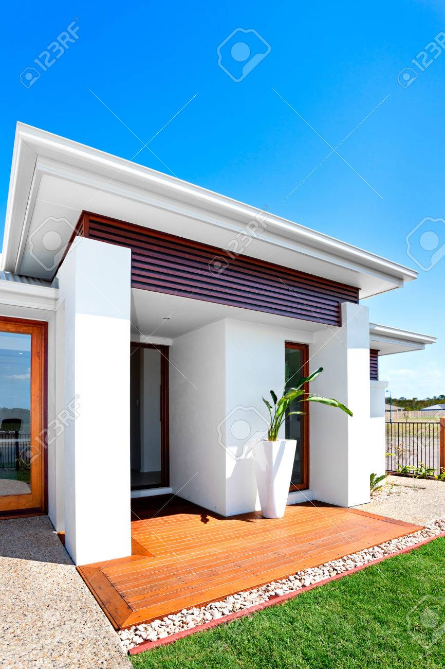 Outdoor of a modern house with green lawn front view from the left side of the house there is a wooden floor and plant with a tall vase of the entrance