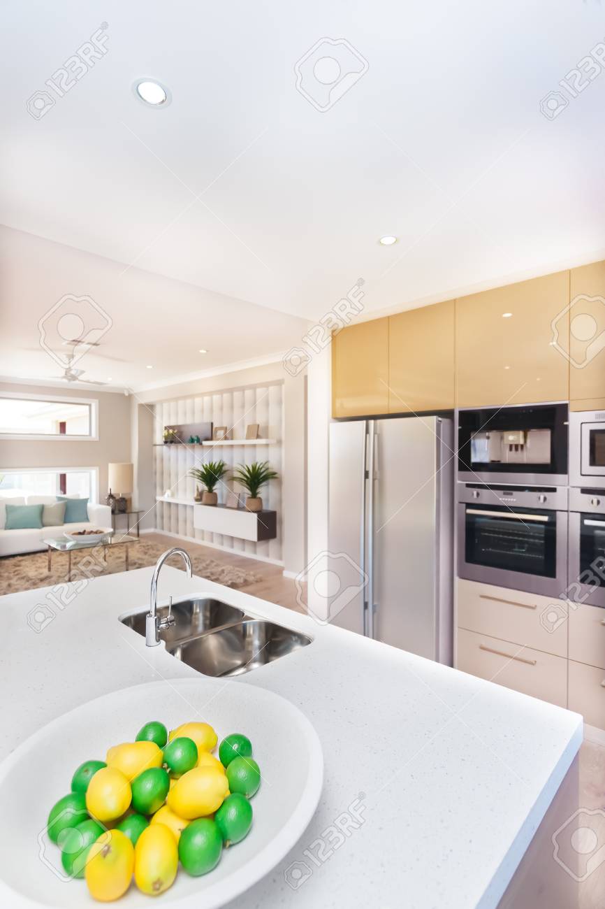 家の中の豪華なキッチン 冷蔵庫と食器棚を壁にマウント パントリーとオーブン ホワイト ワークトップの蛇口と洗面台の近くにレモンのようなプレートにフルーツがあります よくある料理の隣の部屋の装飾 の写真素材 画像素材 Image