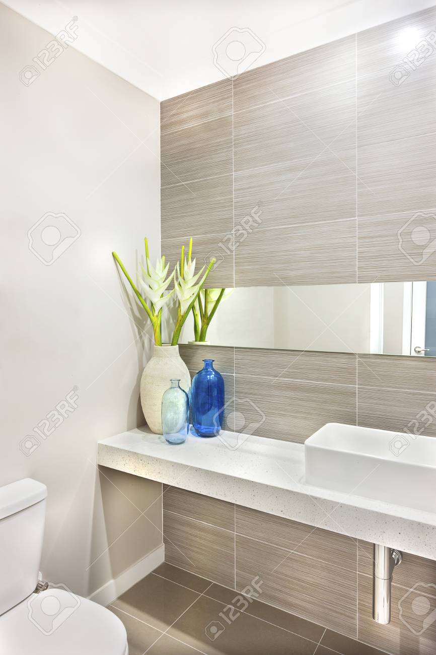 洗うエリアとトイレ白い洗面台近くにカウンターに青いガラスの瓶を用いた光 カラフルな花瓶と白い花を飾られています ミラーは 花瓶の背後にあるパターンの壁に接続されているバーのようです の写真素材 画像素材 Image