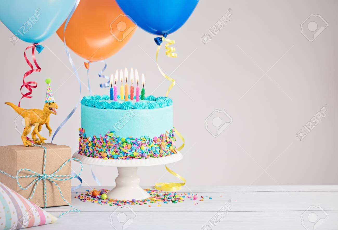 Childs birthday party scene with blue cake, gift box, toy dinosaur, hats and colorful balloons over light grey. - 78949765 Childs birthday party scene with blue cake, gift box, toy dinosaur, hats and colorful balloons over light grey. - 78949765