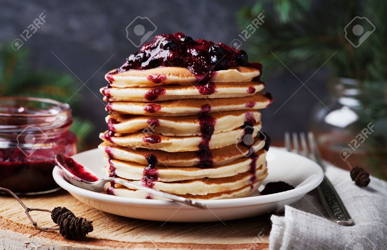 Stack of american pancakes or fritters with strawberry and blueberry jam in white plate on wooden rustic table decorated Christmas tree, delicious dessert for breakfast in winter, vintage style - 50100051 Stack of american pancakes or fritters with strawberry and blueberry jam in white plate on wooden rustic table decorated Christmas tree, delicious dessert for breakfast in winter, vintage style - 50100051