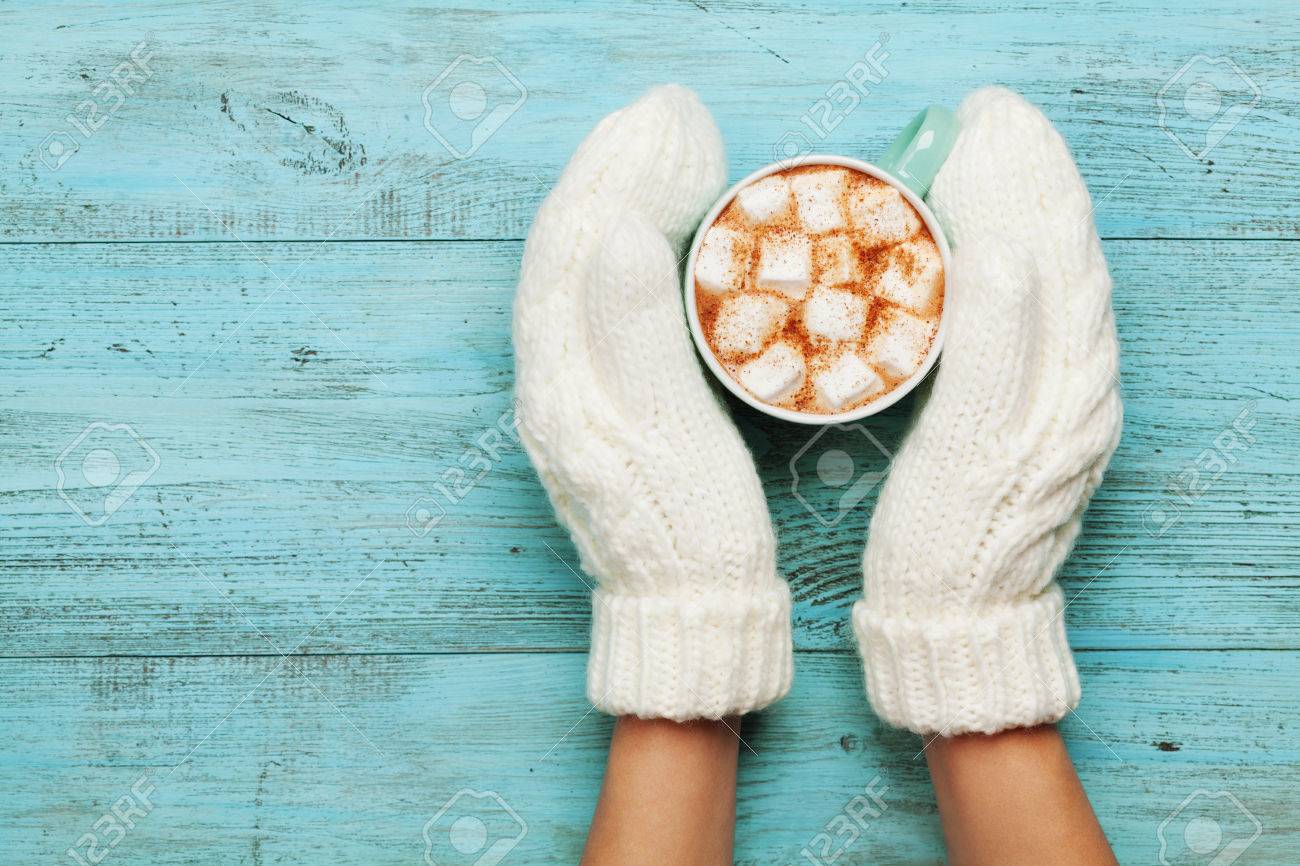 Woman hands in mittens hold cup of hot cocoa or chocolate with marshmallow on turquoise vintage table from above. Flat lay style. - 63908002 Woman hands in mittens hold cup of hot cocoa or chocolate with marshmallow on turquoise vintage table from above. Flat lay style. - 63908002