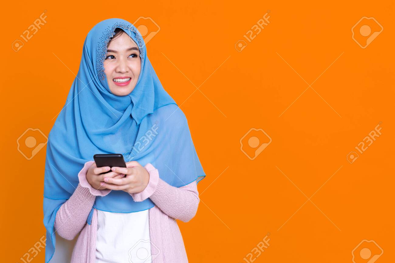 Photo of islamic woman in hijab headscarf wearing mask with oriental makeup use smartphone and credit card over orrange isolate background - 148856618 Photo of islamic woman in hijab headscarf wearing mask with oriental makeup use smartphone and credit card over orrange isolate background - 148856618