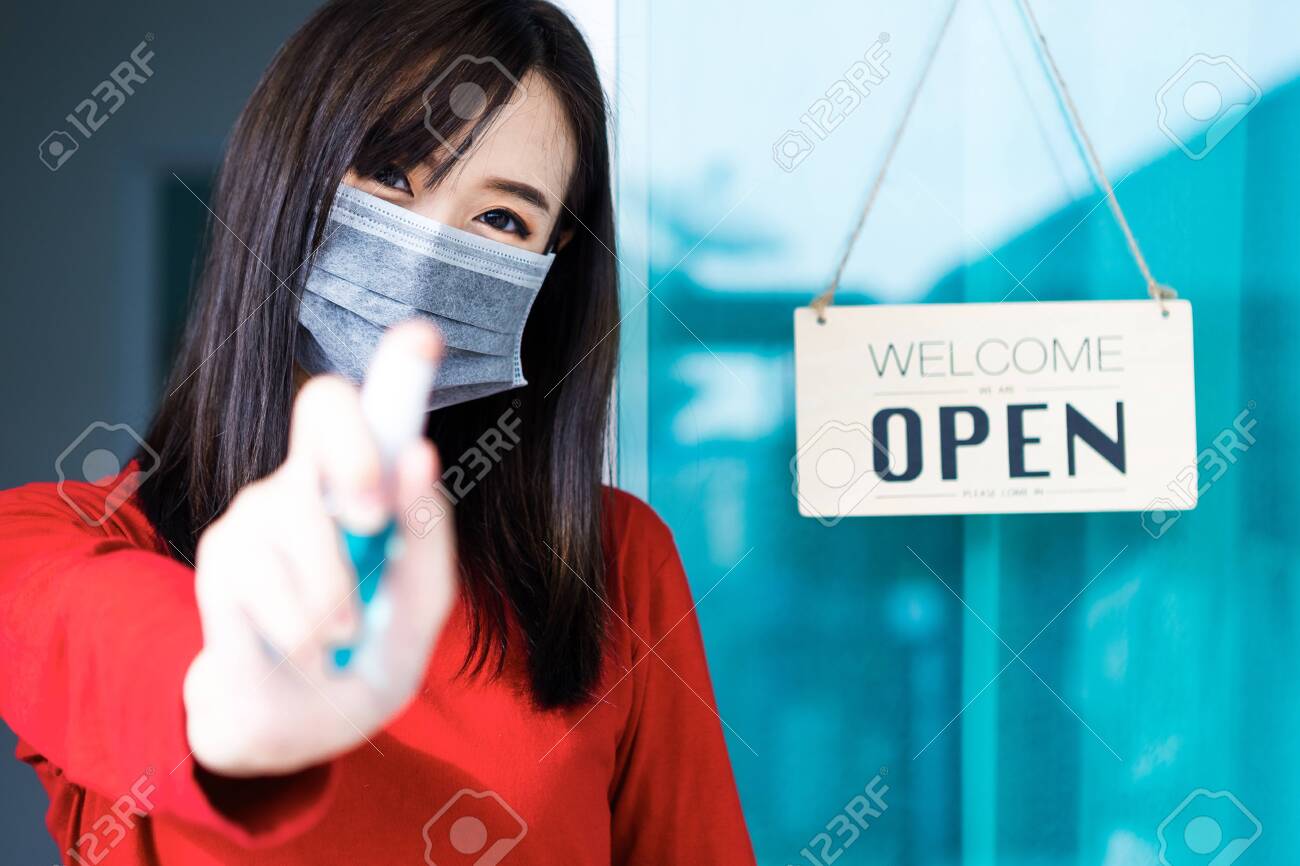 Asian woman shop owner smiling hanging label 'Welcom we are open' and showing thump up. She open her shop after pandemic of coronavirus outbreak - 149473799 Asian woman shop owner smiling hanging label 'Welcom we are open' and showing thump up. She open her shop after pandemic of coronavirus outbreak - 149473799