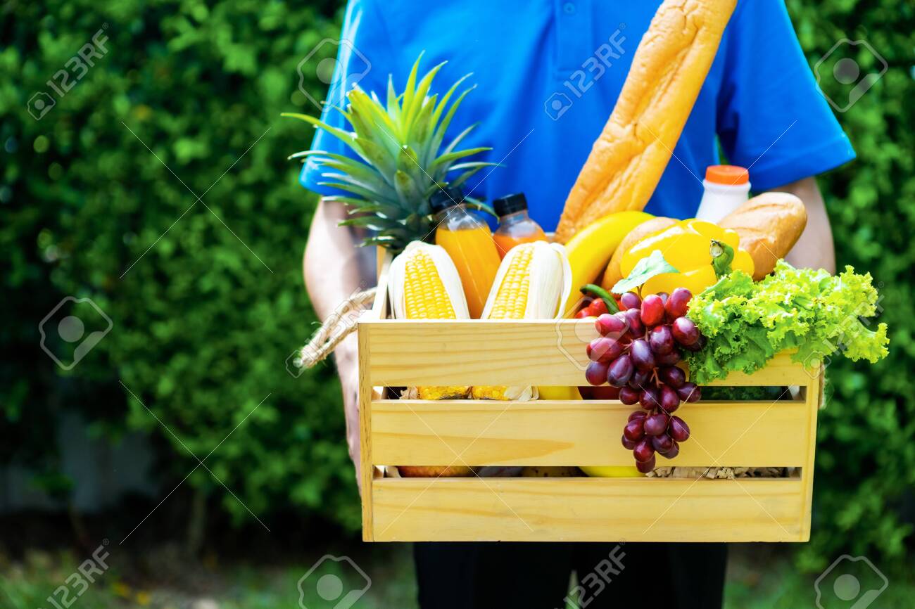 Asian delivery man blue uniform wearing medical face mask making grocery service giving fresh food to customer receiving front house, Food delivery and grocery service concept. - 149473805 Asian delivery man blue uniform wearing medical face mask making grocery service giving fresh food to customer receiving front house, Food delivery and grocery service concept. - 149473805