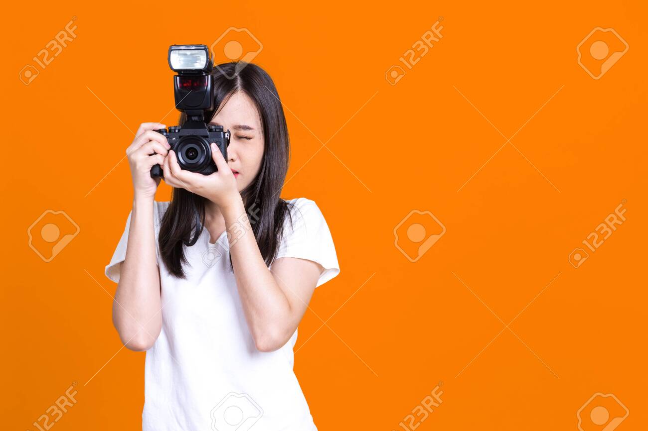 Portrait photo of Asian smiling pretty girl in white shirt taking photo on camera isolated over color background - 149473878 Portrait photo of Asian smiling pretty girl in white shirt taking photo on camera isolated over color background - 149473878