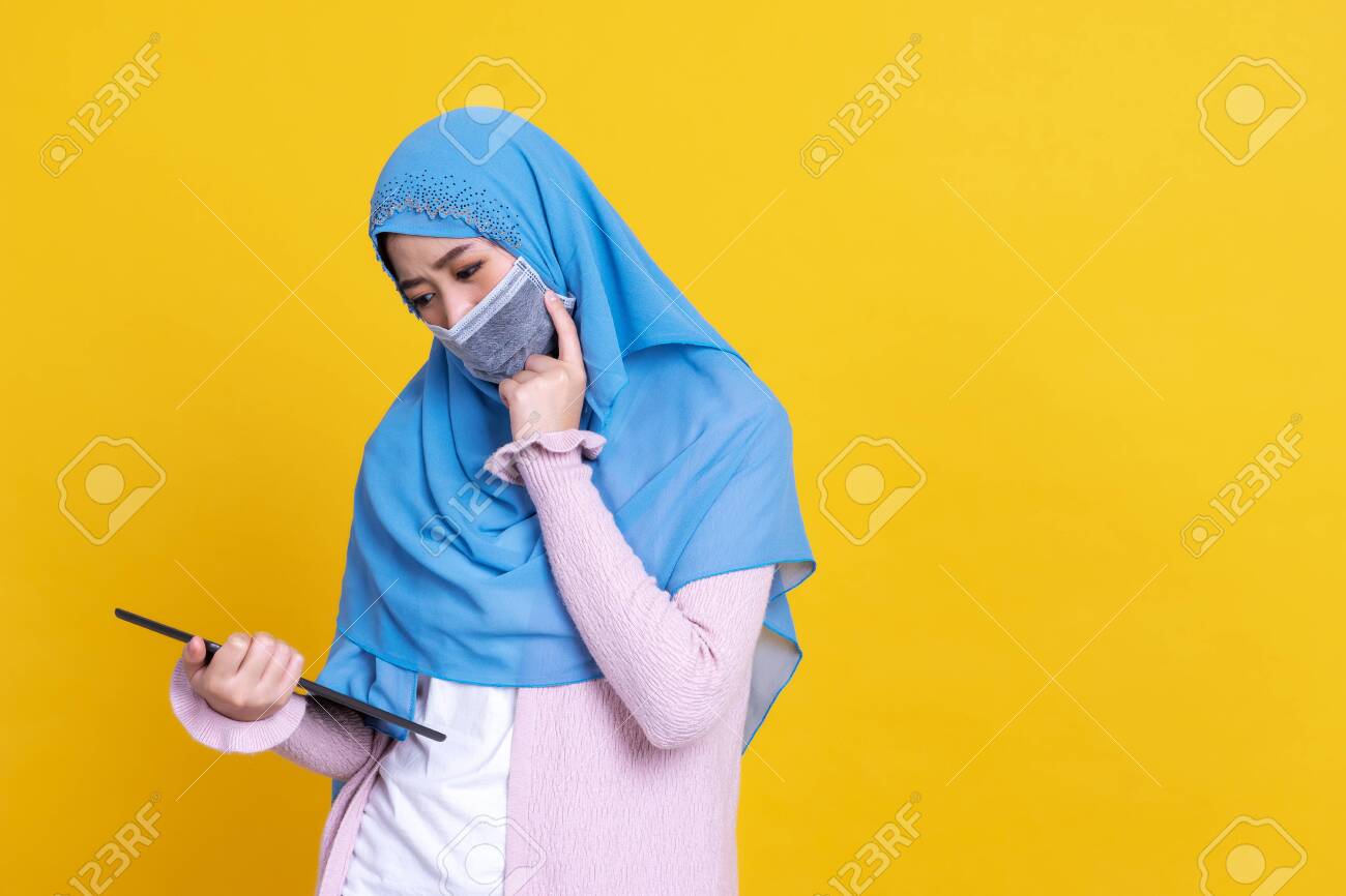 Asian Muslim woman wearing medical mask in hijab and using digital tablet isolated on color background - 149473944 Asian Muslim woman wearing medical mask in hijab and using digital tablet isolated on color background - 149473944