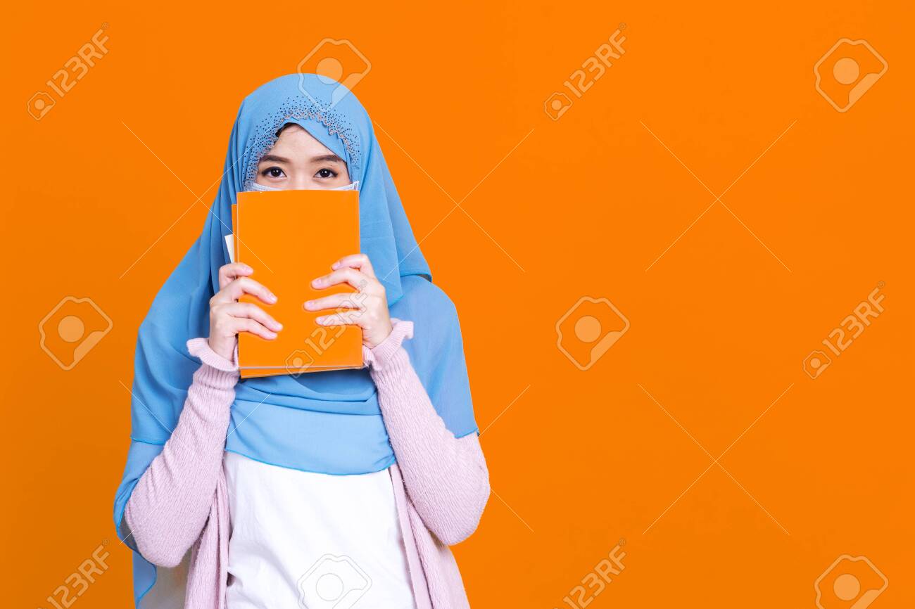 Asian muslim woman in hijab and wearing medical mask and holding book over isolate color background. Education concept. - 149473953 Asian muslim woman in hijab and wearing medical mask and holding book over isolate color background. Education concept. - 149473953