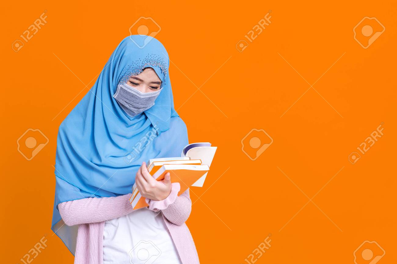 Asian muslim woman in hijab and wearing medical mask and holding book over isolate color background. Education concept. - 149473956 Asian muslim woman in hijab and wearing medical mask and holding book over isolate color background. Education concept. - 149473956