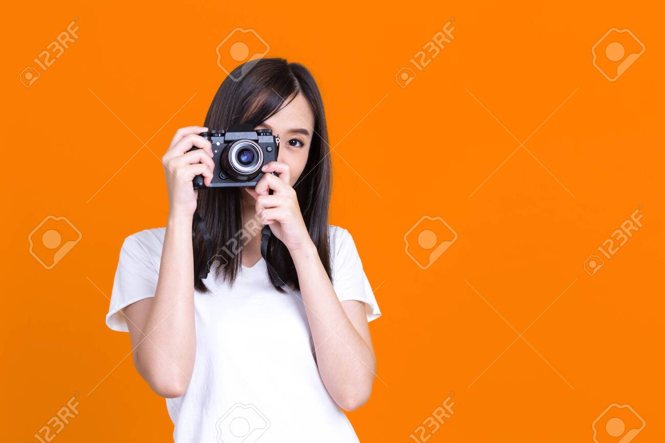 Asian woman smiling pretty girl in white shirt taking photo on camera isolated over color background - 149474083 Asian woman smiling pretty girl in white shirt taking photo on camera isolated over color background - 149474083