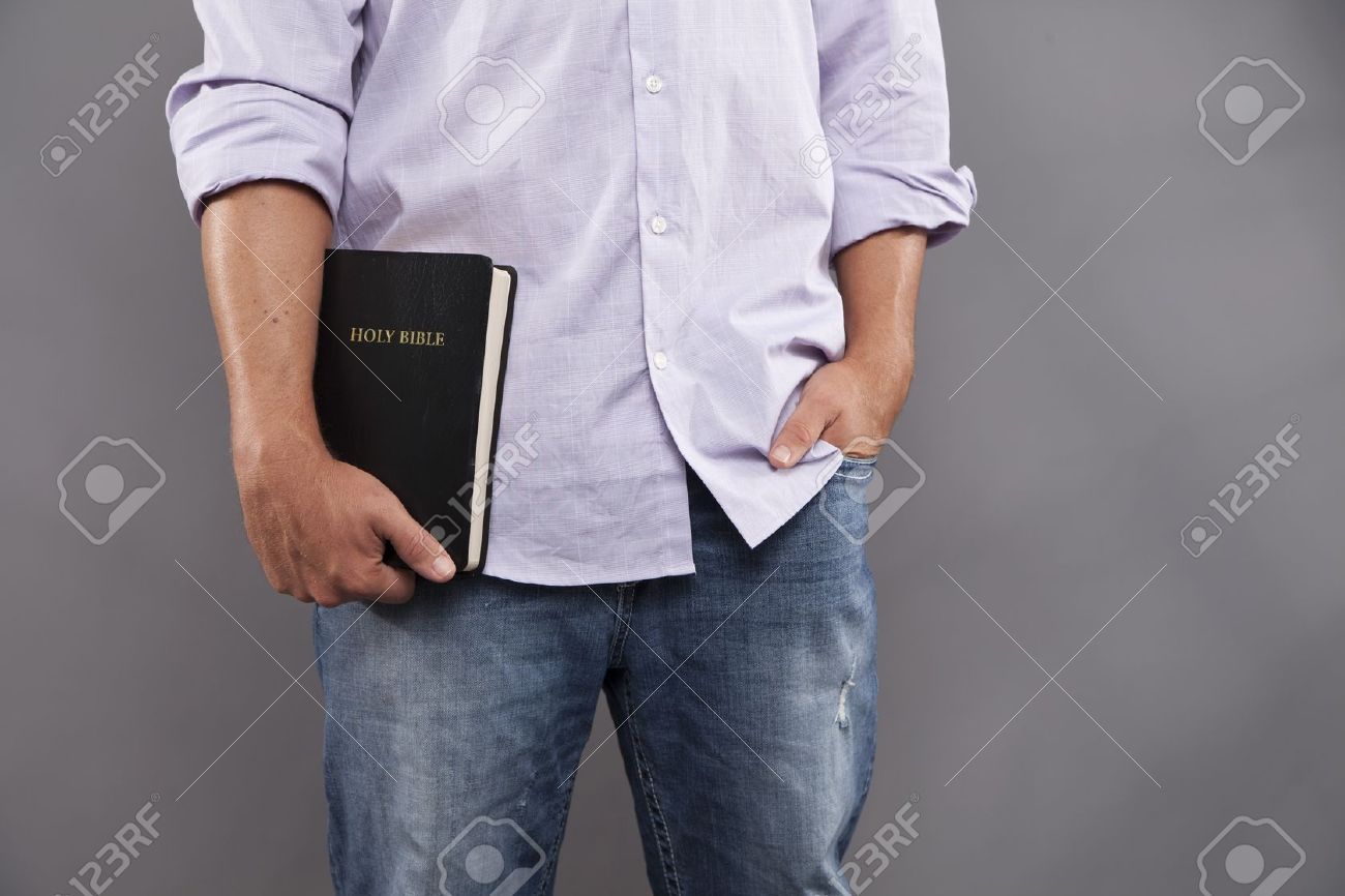 A Man Stands Indoors With One Hand Holding A Black Bible And