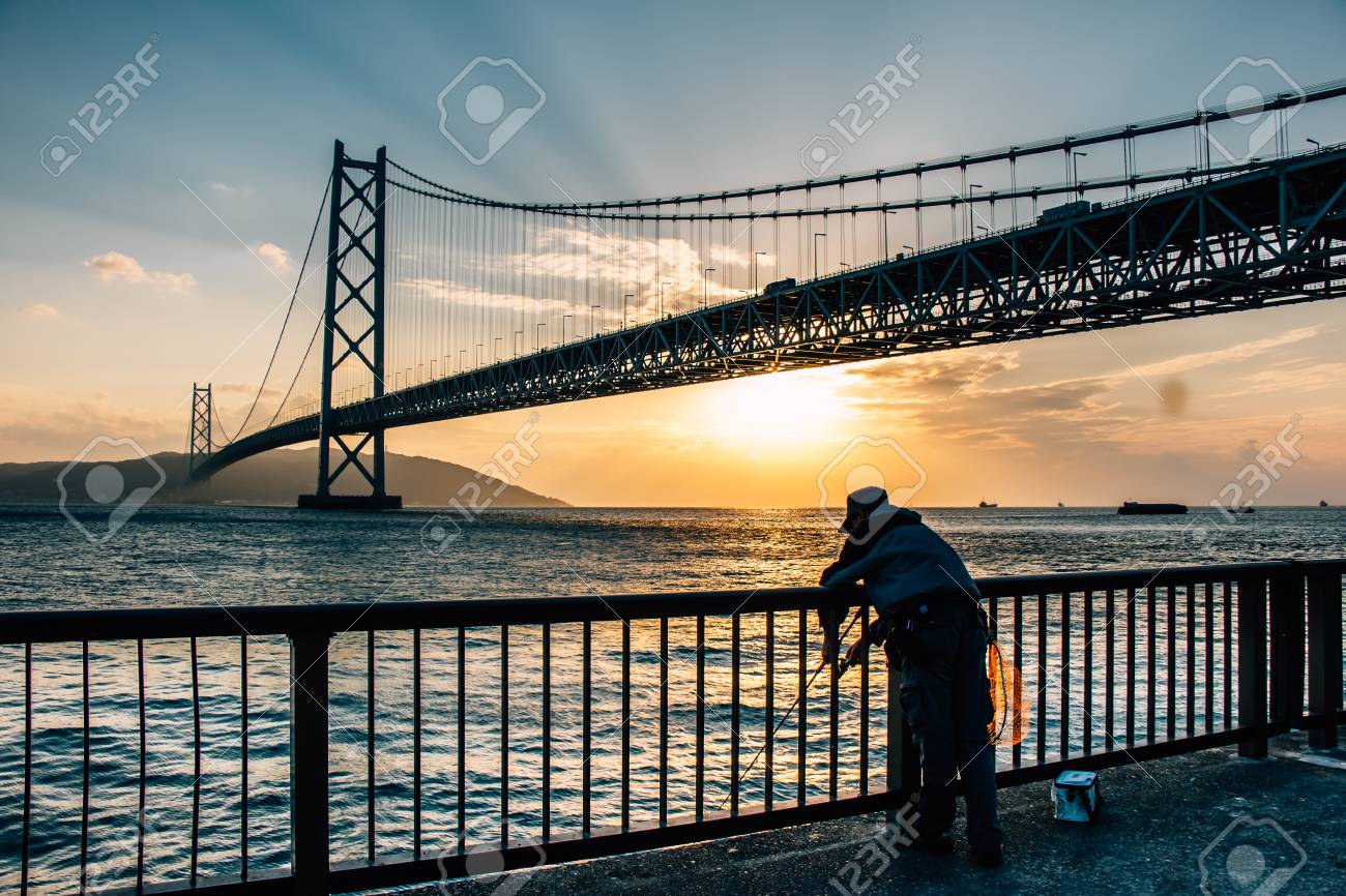 吊橋である明石海峡大橋で橋と夕日の底面で釣り 瀬戸内海を淡路島から神戸市にまたがる男のシルエット の写真素材 画像素材 Image