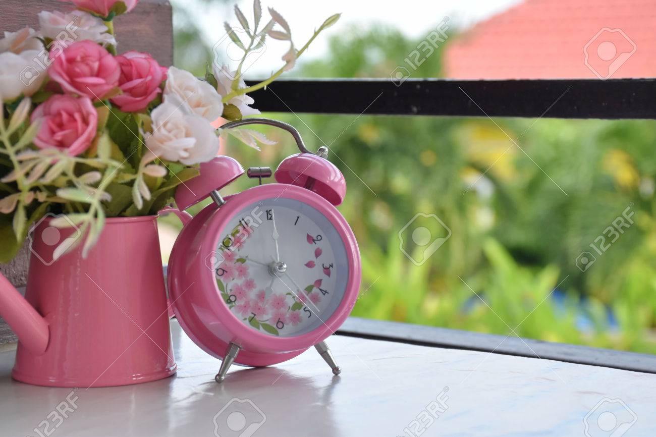 pink alarm clock and rose flowers in vase on white table in stock