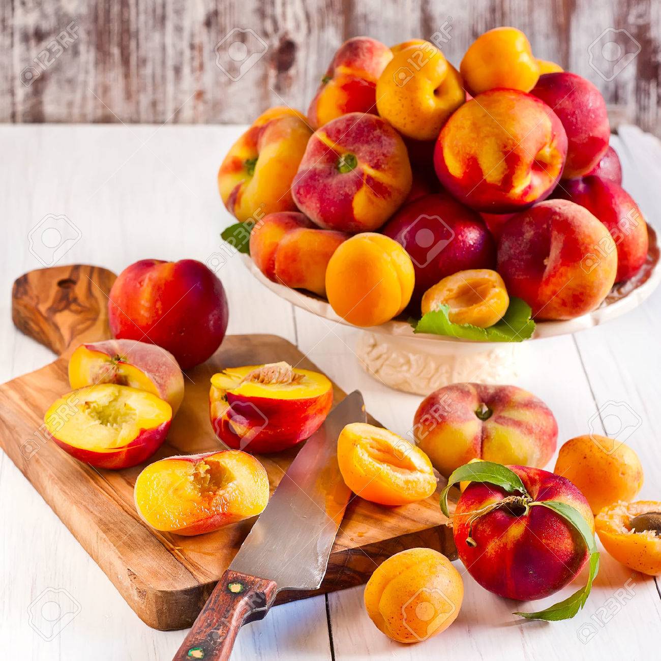 Ripe apricots, nectarines and saturn peaches on ceramic holder and olive wood desk with knife. - 29207544 Ripe apricots, nectarines and saturn peaches on ceramic holder and olive wood desk with knife. - 29207544