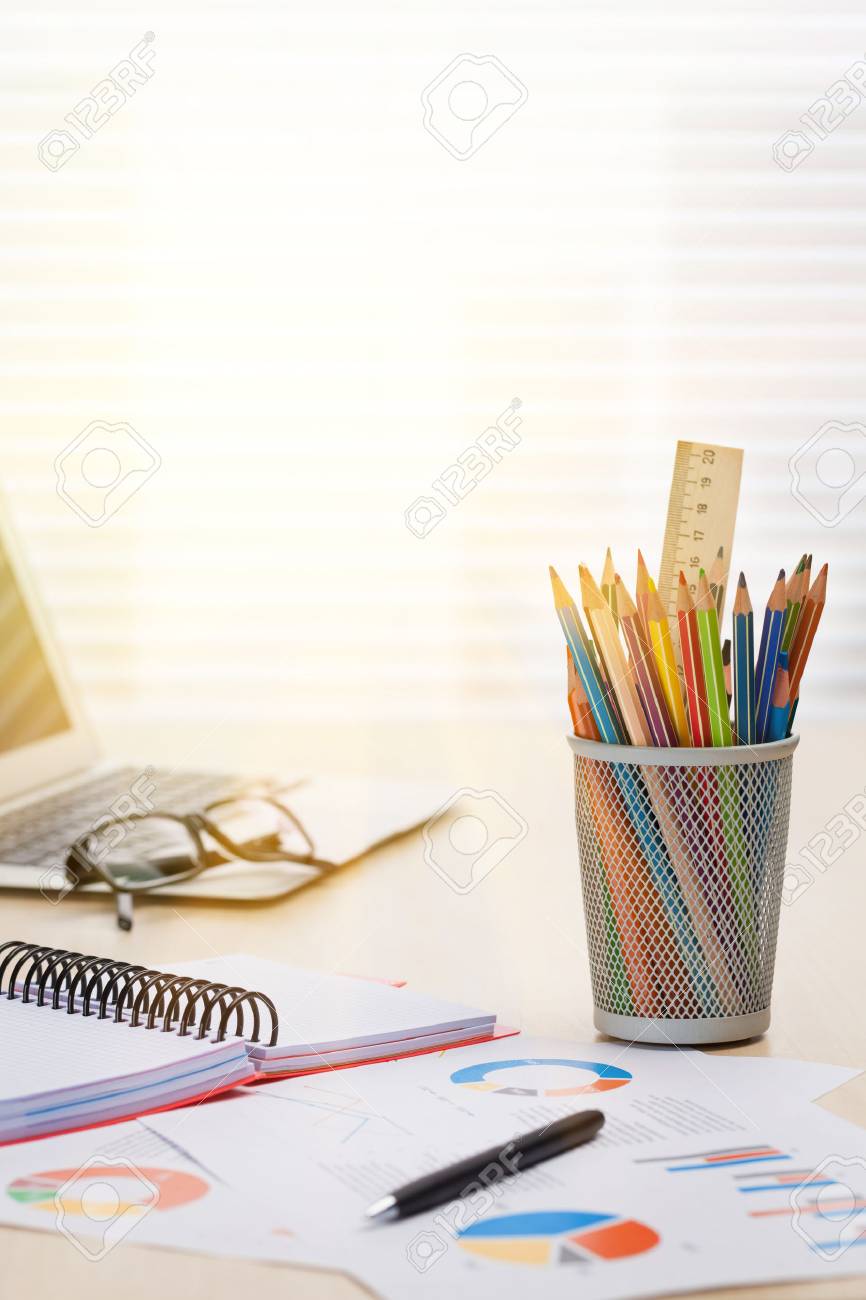 オフィス ブラインドのある窓の前で木製のデスク テーブルの上に鉛筆やノート パソコン レポートと職場 夕日の光 の写真素材 画像素材 Image