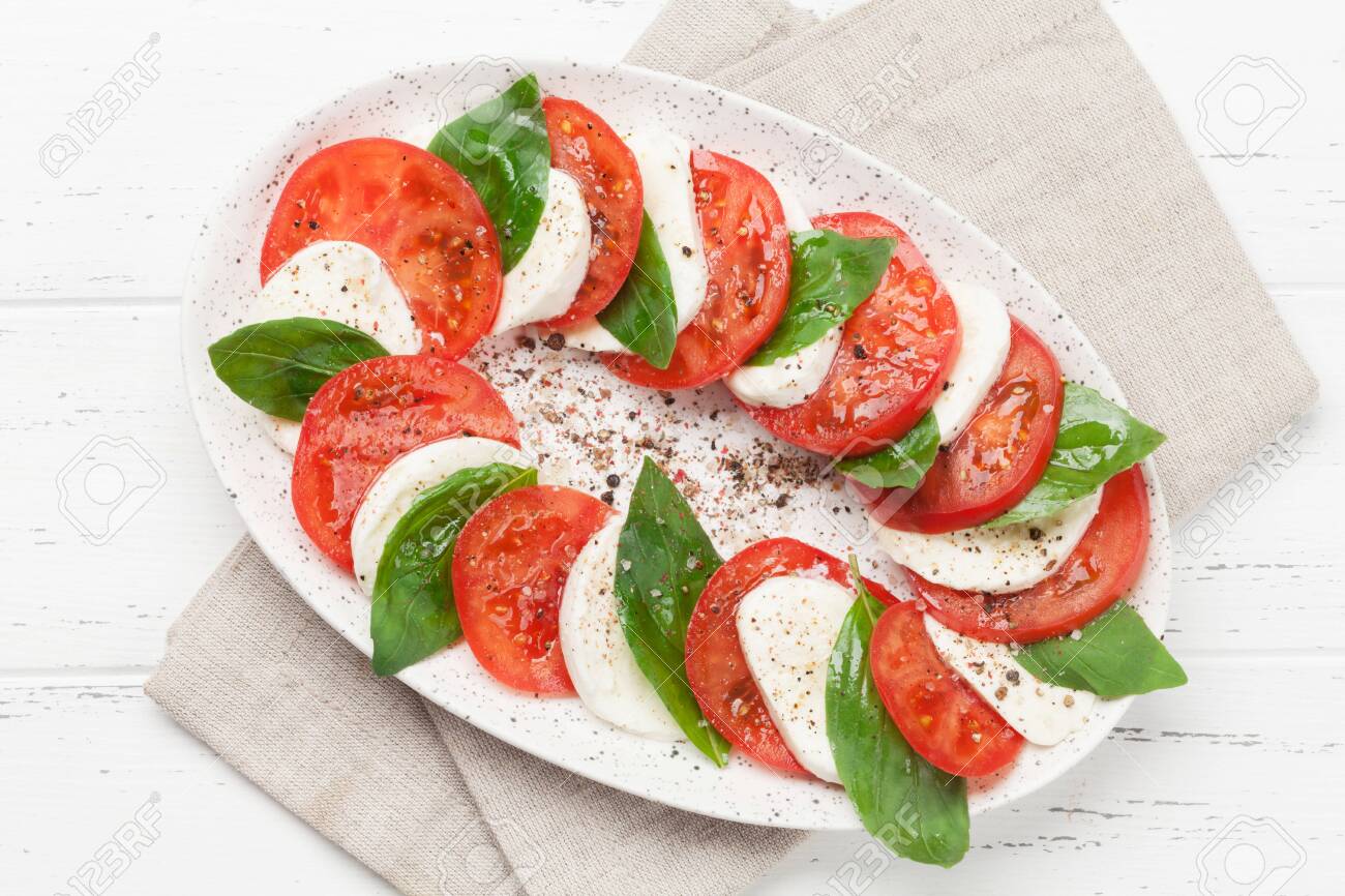 Delicious italian caprese salad with ripe tomatoes, fresh garden basil and mozzarella cheese. Top view flat lay - 120470408 Delicious italian caprese salad with ripe tomatoes, fresh garden basil and mozzarella cheese. Top view flat lay - 120470408