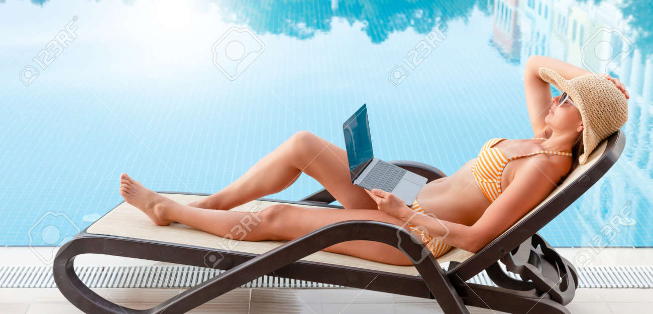 Young woman using laptop for remote work or education near a swimming pool. With copy space for your text or app - 169317590 Young woman using laptop for remote work or education near a swimming pool. With copy space for your text or app - 169317590