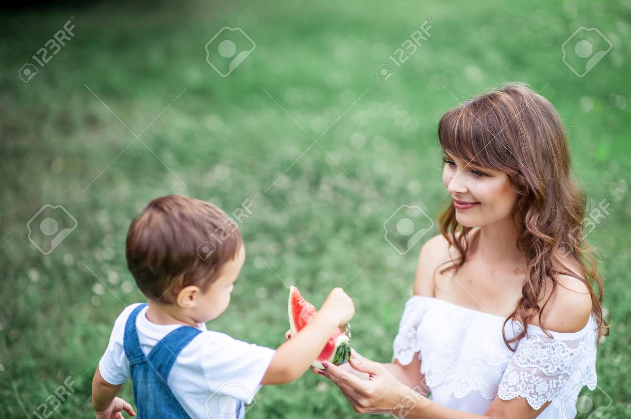 若いお母さんと幼い息子は 草で再生 幸せなお母さんと息子草の上に座るし スイカを食べる 夏 の写真素材 画像素材 Image