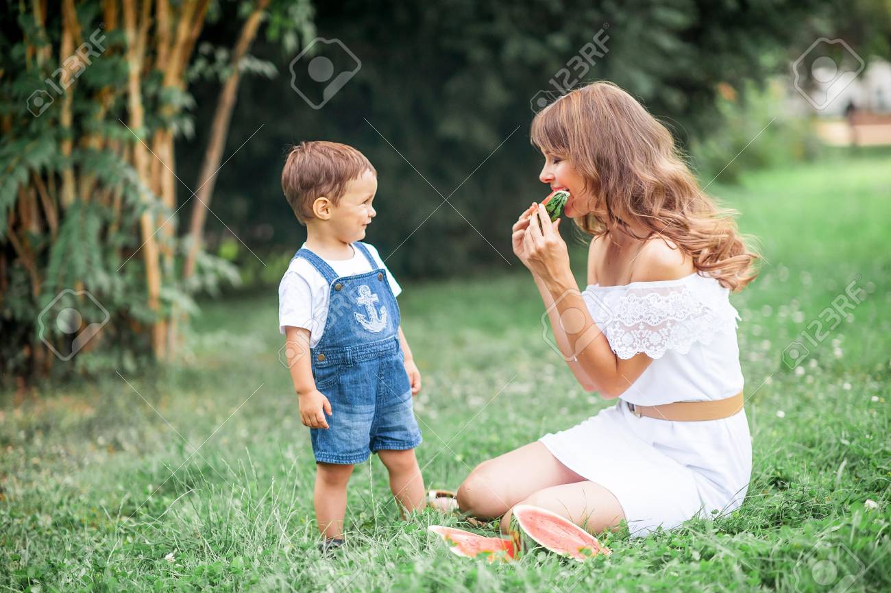 若いお母さんと幼い息子は 草で再生 幸せなお母さんと息子草の上に座るし スイカを食べる 夏 の写真素材 画像素材 Image