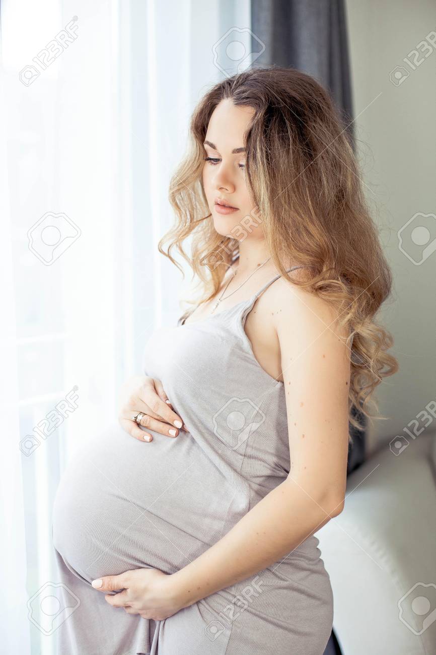 Immagini Stock - Una Giovane Bella Donna Incinta È In Piedi Vicino Alla  Finestra. Incinta In Un Bellissimo Vestito. Maternità. Gravidanza. Ritratto  Di Una Donna Incinta Felice. Accogliente.. Image 97715385