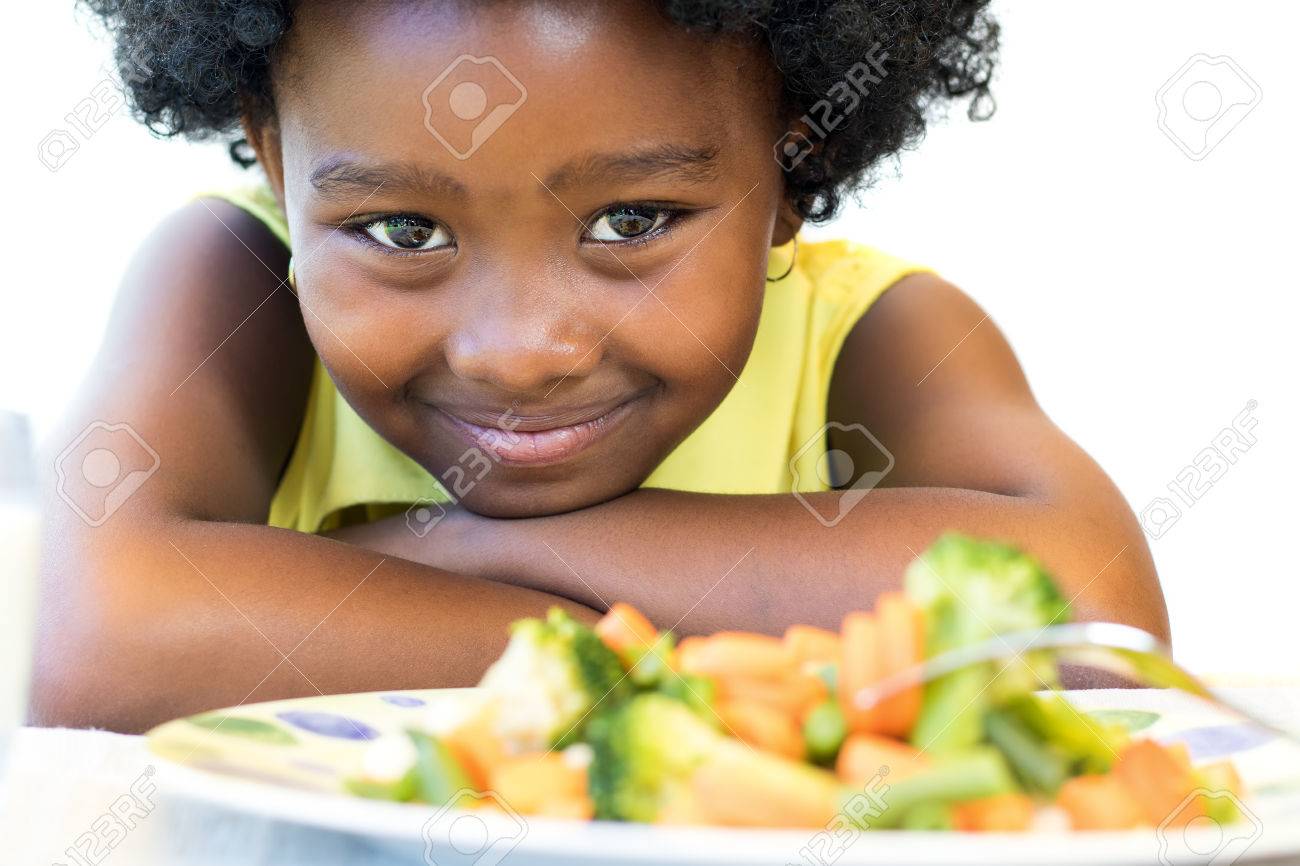 Close up face shot of cute African girl in front of healthy vegetable dish. Isolated on white. - 66647649 Close up face shot of cute African girl in front of healthy vegetable dish. Isolated on white. - 66647649