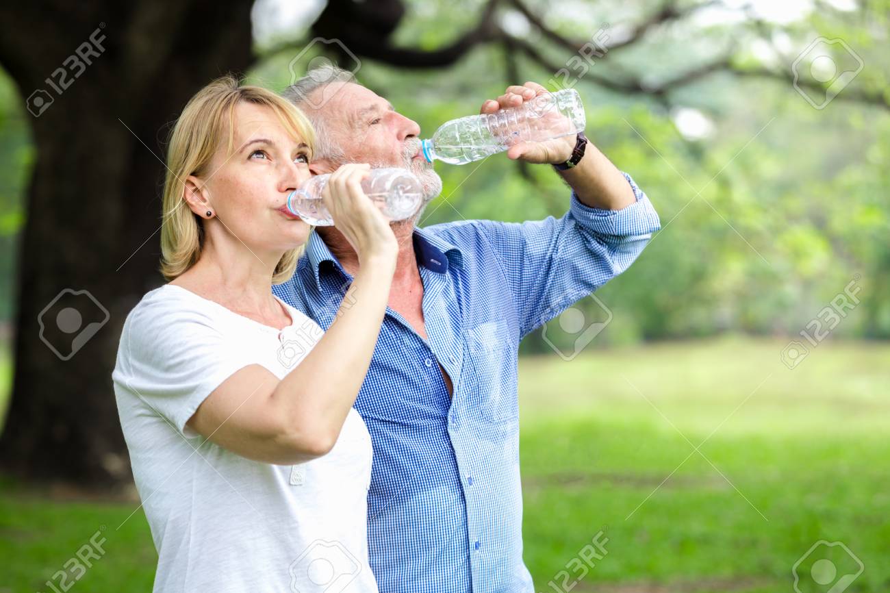 Portrait senior couple standing drinking water at the park - 96513323 Portrait senior couple standing drinking water at the park - 96513323