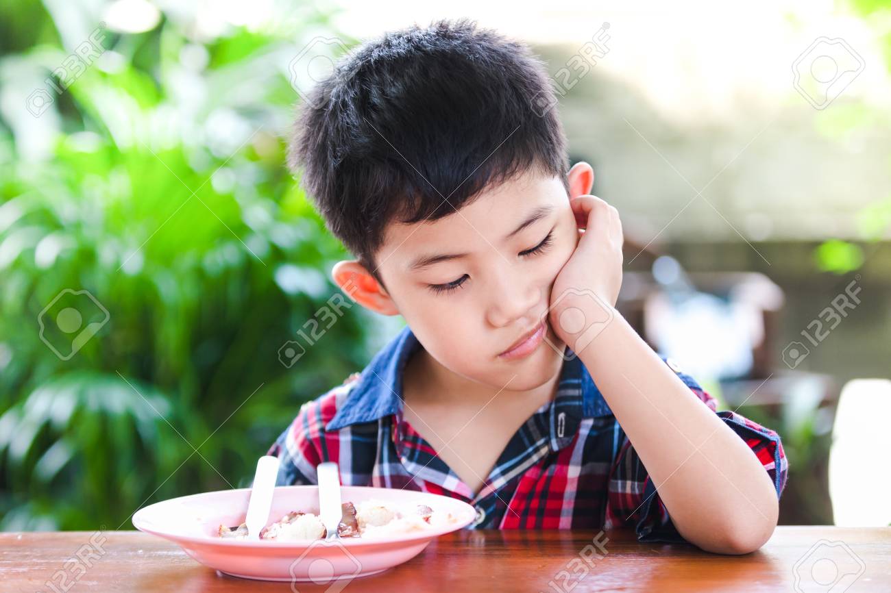 Asian little boy boring eating with rice food on the wooden table - 99408045 Asian little boy boring eating with rice food on the wooden table - 99408045