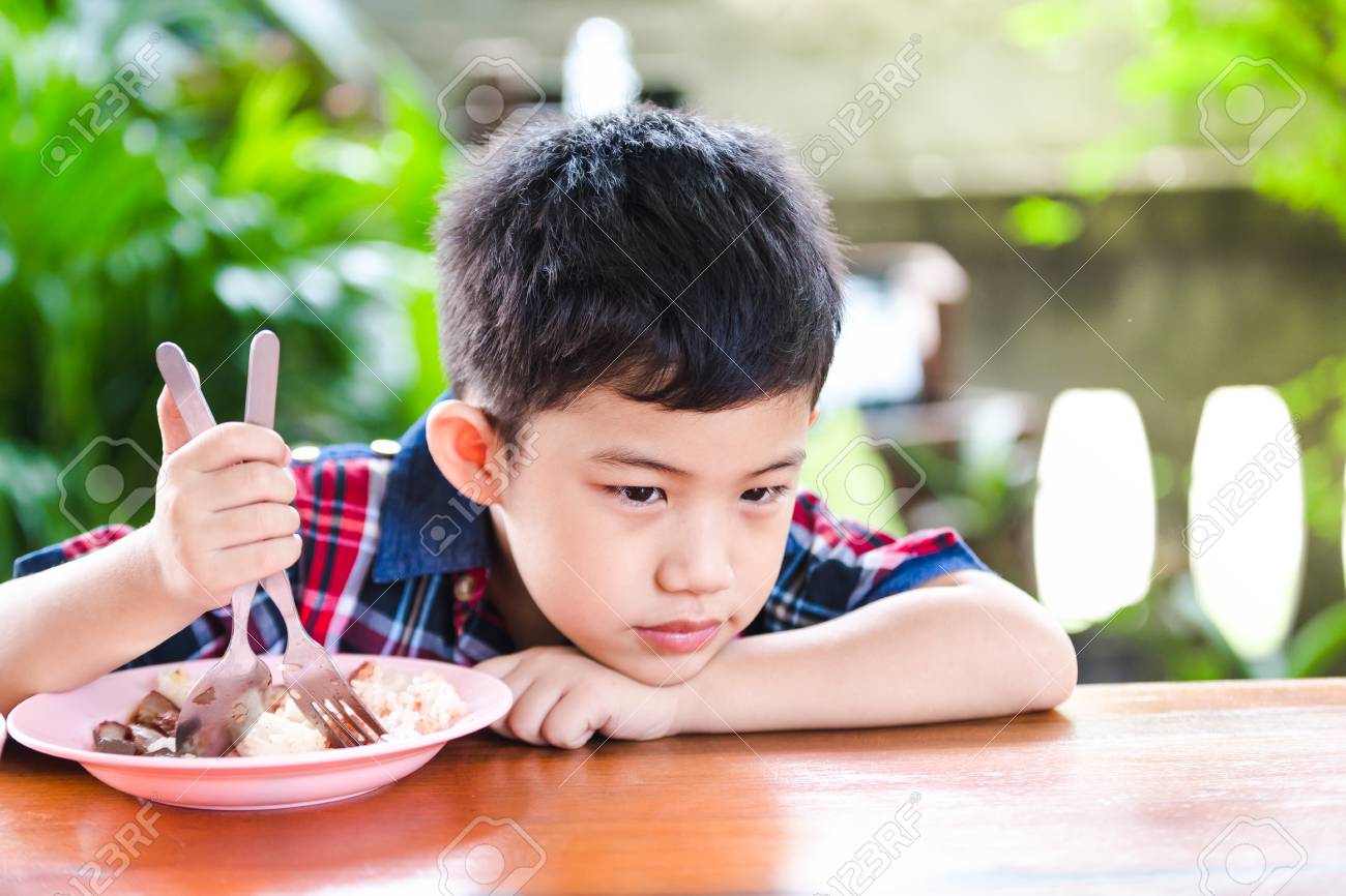Asian little boy boring eating with rice food on the wooden table - 102279992 Asian little boy boring eating with rice food on the wooden table - 102279992