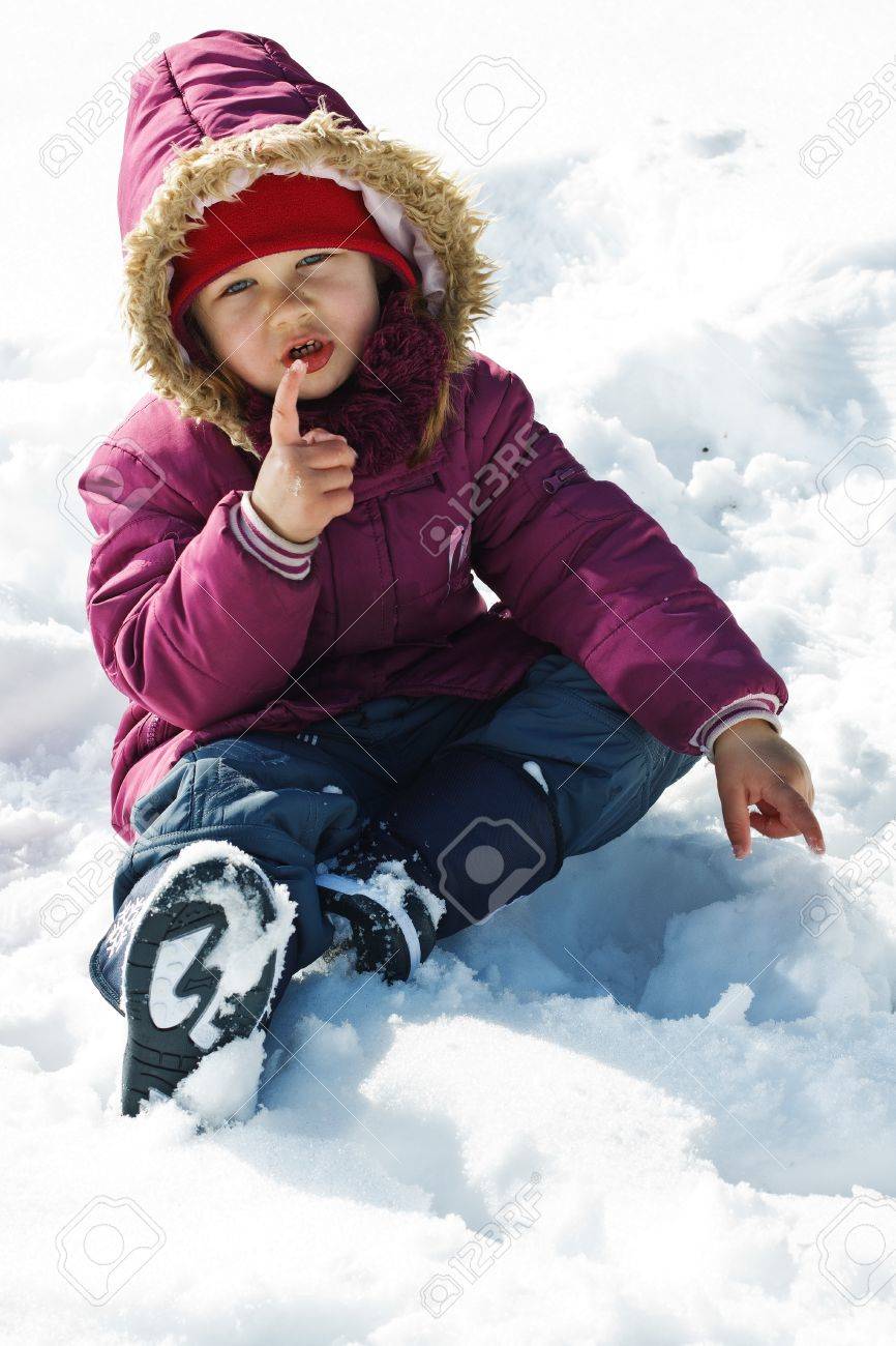 かわいい 3 歳女の子は屋外で遊ぶ 冬服 雪の中で座っているカメラに探している 彼女の指を指しているの肖像画 の写真素材 画像素材 Image