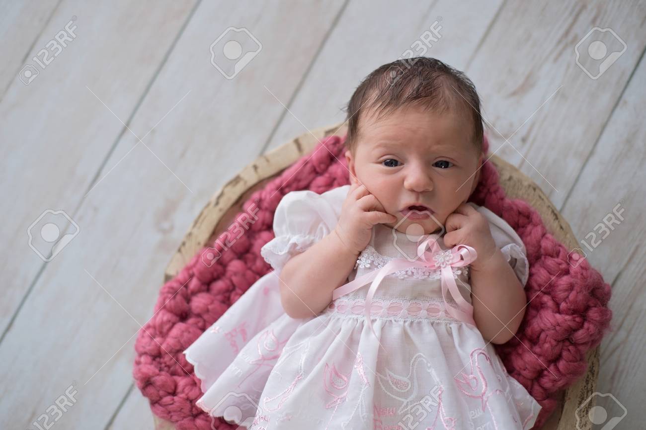 木製のボウルに横になっているアラート 生後 10 日の新生児の赤ちゃんの女の子 フリルの白とピンクのドレスを着ています 明るい木製の背景のスタジオで撮影します の写真素材 画像素材 Image