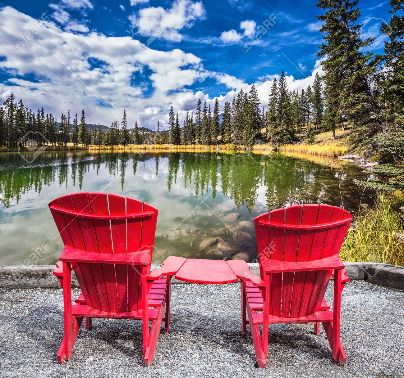 two red plastic chairs on the lake on shores of the lake grow