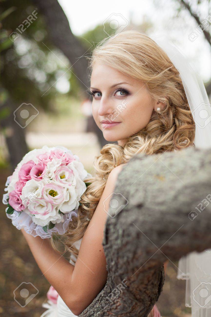 Attractive bride posing in the green leaves of the tree in her wedding day - 17152779 Attractive bride posing in the green leaves of the tree in her wedding day - 17152779