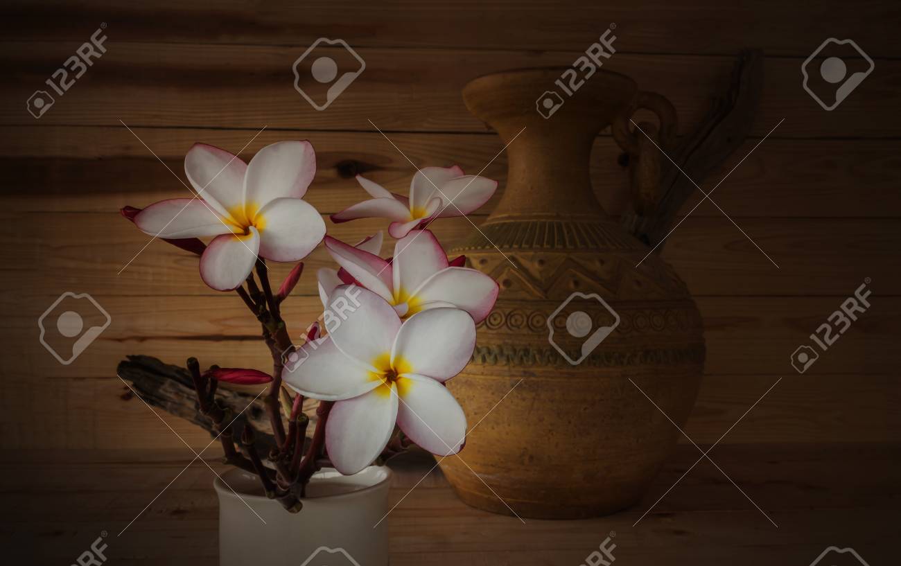 ソフトのセピア色とアンティーク色のトーン 古いヴィンテージの焼かれた粘土の花瓶と木の背景と甘いピンク黄色白い花プルメリアやフランジパニの束 の写真素材 画像素材 Image