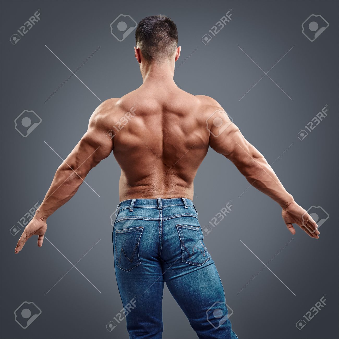 male bodybuilder flexing his back muscles on grey background