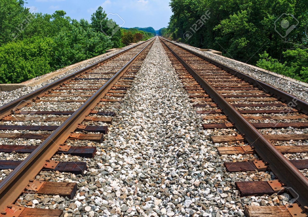 Two sets of railroad tracks run straight and parallel to a vanishing point on the horizon with green trees along side - 21266853 Two sets of railroad tracks run straight and parallel to a vanishing point on the horizon with green trees along side - 21266853
