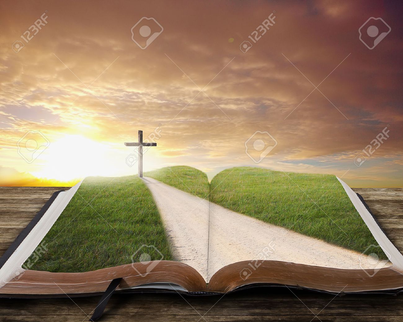 An open Bible with a road and grassy field leading to a cross. - 27594898 An open Bible with a road and grassy field leading to a cross. - 27594898