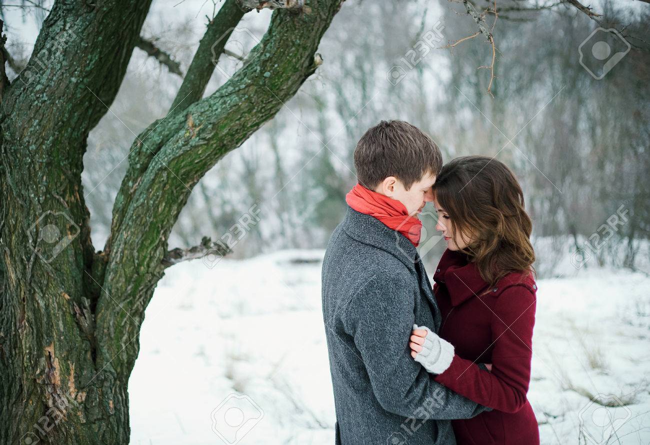 L Homme Embrasse Tendrement Belle Fille Ils Se Tiennent Sur Une Prairie Couverte De Neige A Un Arbre Enorme L Amour De Deux Coeurs Promenade D Hiver Scenic Dans Le Parc Un Sentiment Romantique Tir