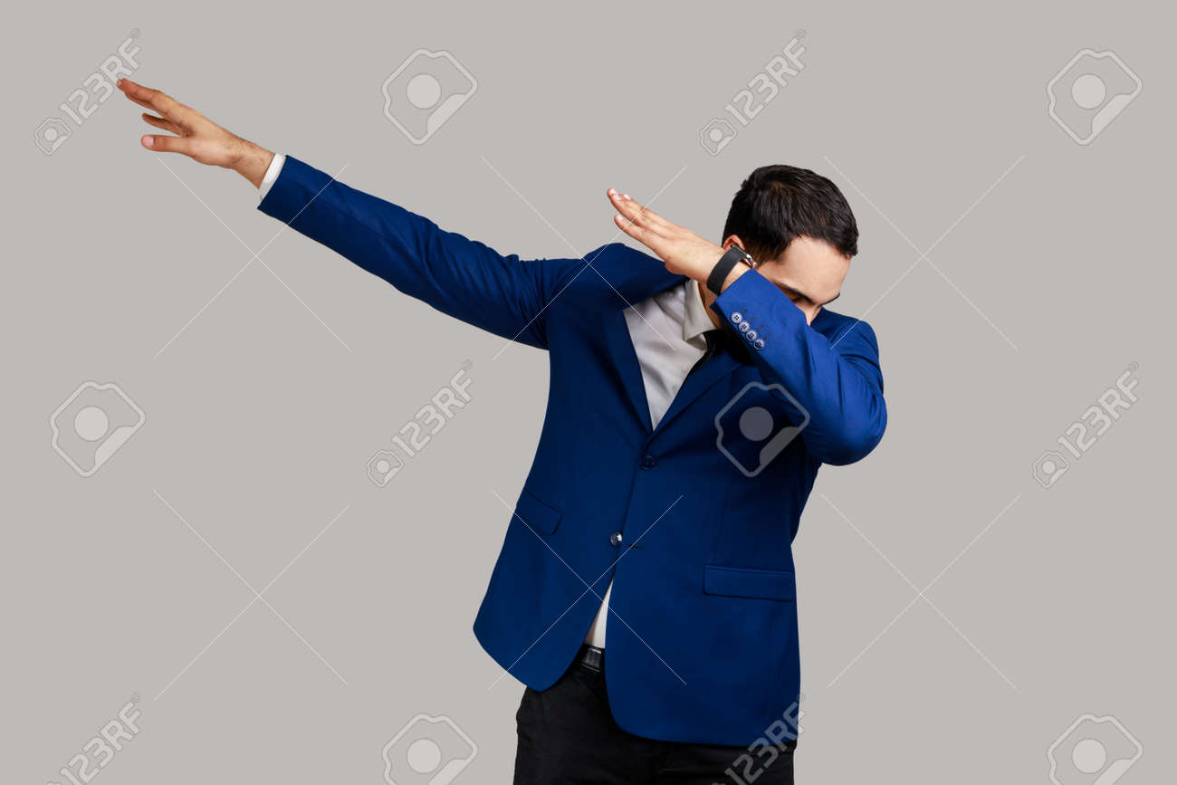 ダブダンスポーズ、インターネットミーム、成功を祝い、公式スタイルのスーツを着て立つポジティブな楽観的なビジネスマンのポートレート。グレイの背景に屋内スタジオショット。の写真素材・画像素材  Image 188417754