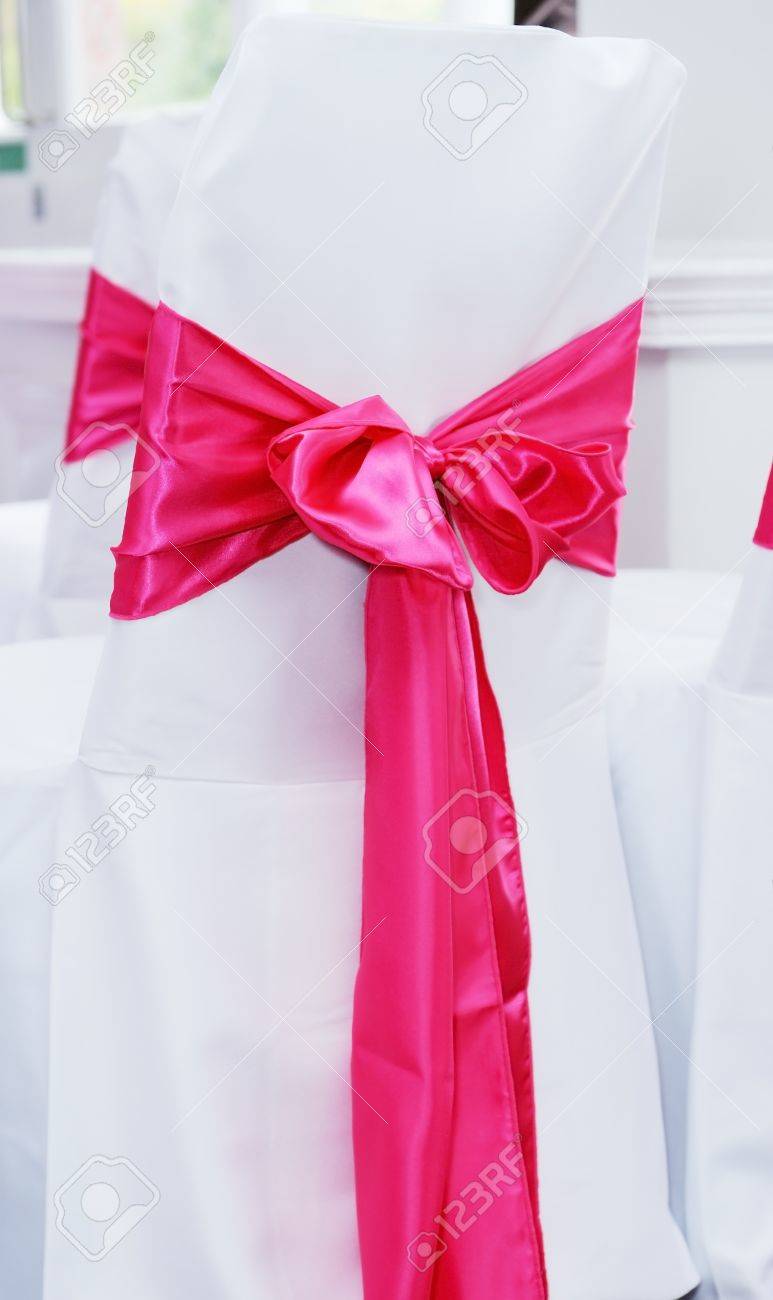 closeup of white chair cover with red or pink ribbon tied in stock