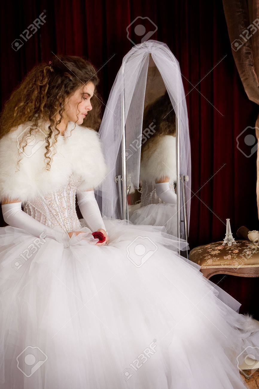 The bride in a beautiful wedding dress with a long curly hair stands in the  bedroom and looks at the camera Bride indoors with white flowers bouquet  Stock Photo  Alamy