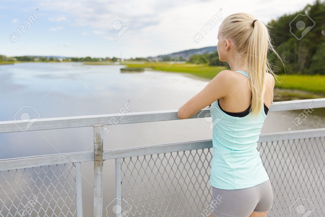 若く美しい金髪女性ジョギングやランニング後休憩に合います 橋の上に立っていると考える彼女ながらフェンスにもたれて の写真素材 画像素材 Image